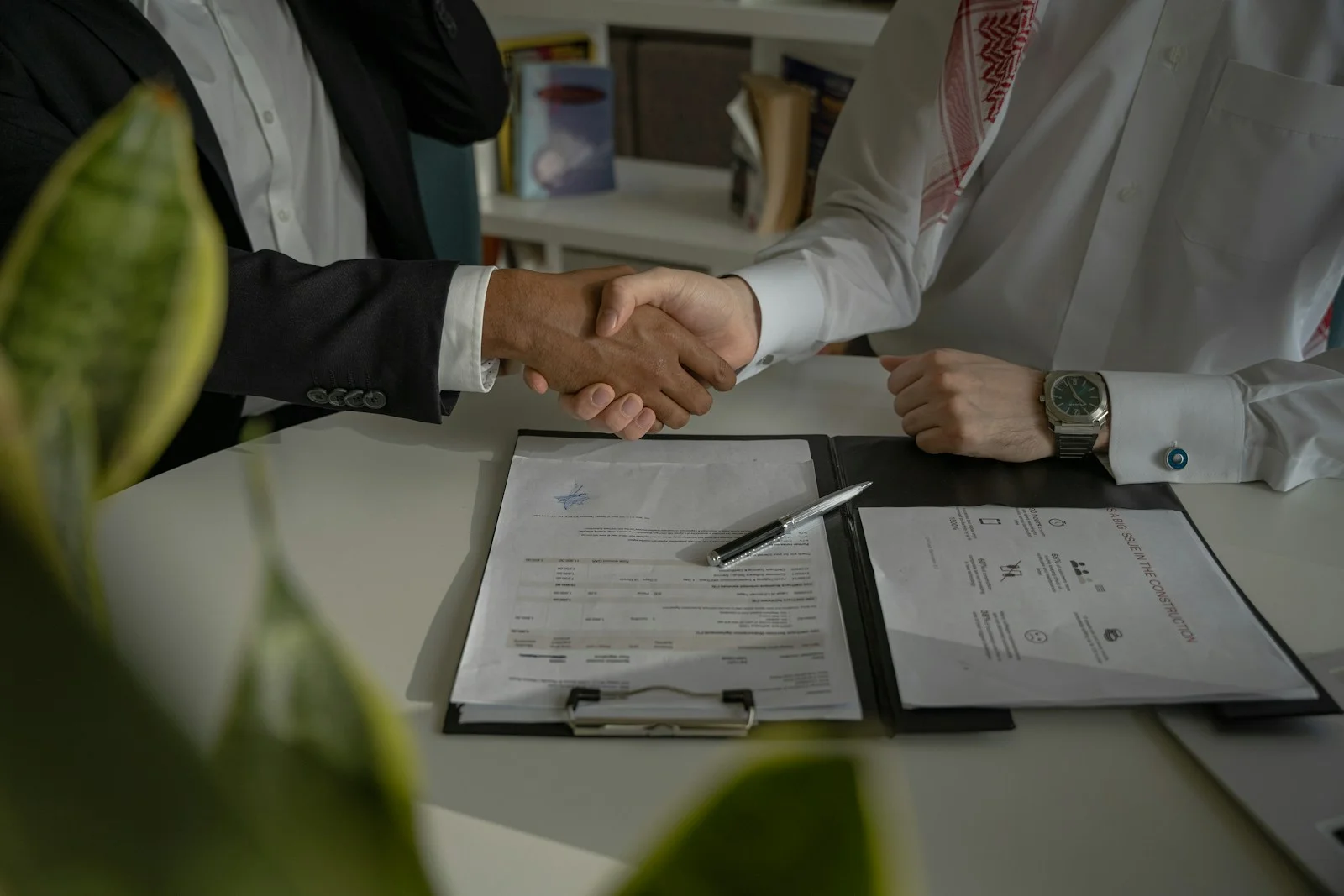 Deux personnes se serrent la main au-dessus d’un contrat posé sur une table